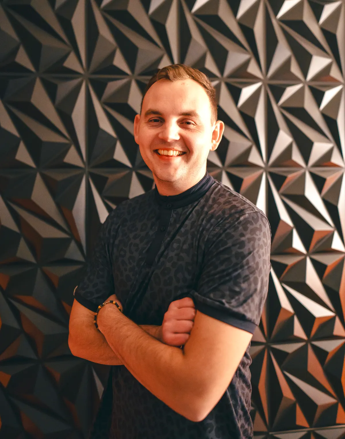 Cory Clark, founder of The Sales Therapist, standing with his arms folded in front of a faceted geometric wall.